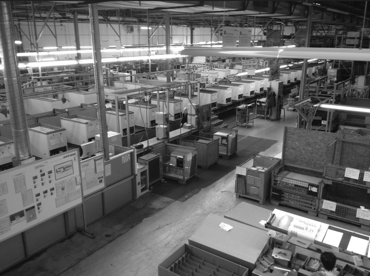 Black-and-white photo of a factory floor with rows of chest freezers on assembly lines