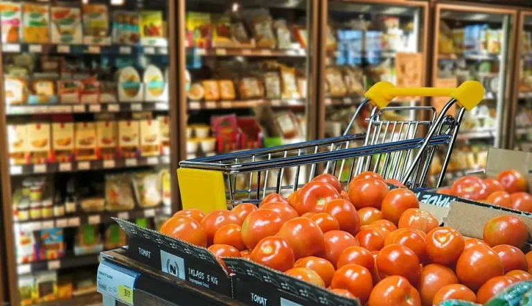 Grocery aisle with a shopping cart and a display of tomatoes in front of refrigerated cases