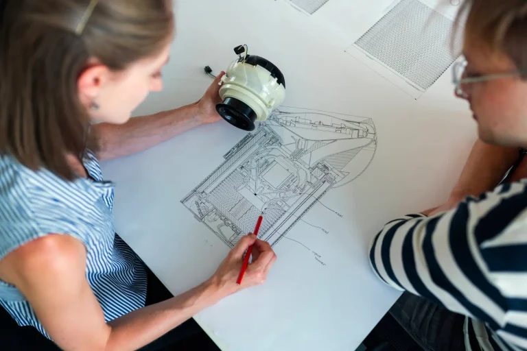 Two designers marking up a technical drawing of a product part